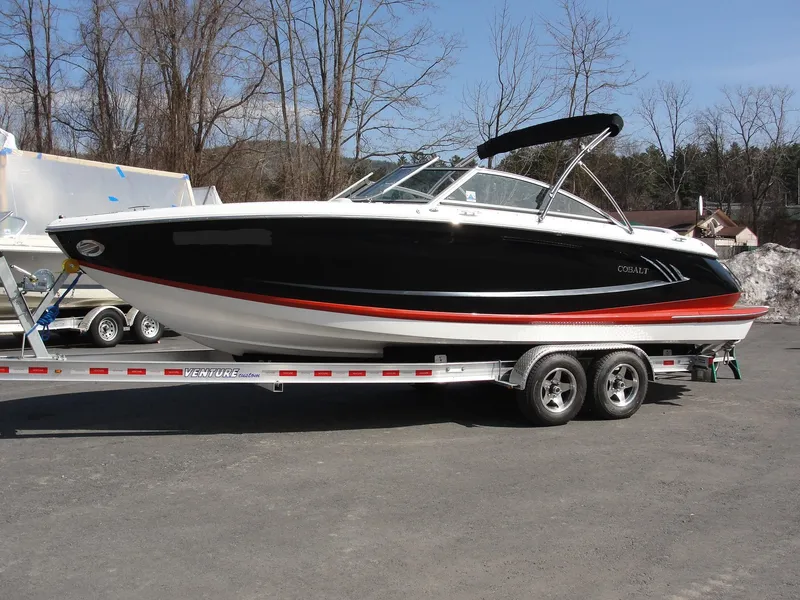 Slide: The Image of 2013 Cobalt A25 boat on trailer, black and red design, parked outdoors. - 1