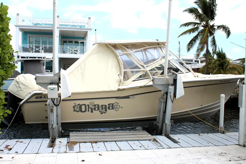 Slide: The Image of 2019 Grady-White Freedom 275 boat docked, covered, with palm trees and a house in the background. - 2