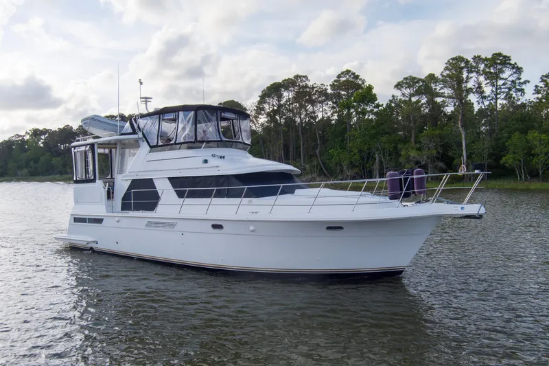 The Image of 1997 Carver 445 Aft Cabin Motor Yacht on serene water with lush green backdrop. - 1