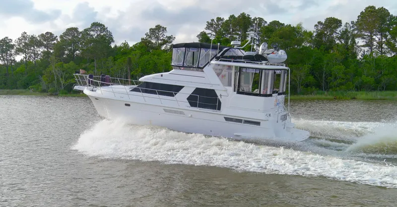 Slide: The Image of 1997 Carver 445 Aft Cabin Motor Yacht cruising on a river with lush green trees. - 22
