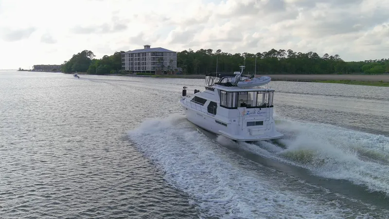 Slide: The Image of 1997 Carver 445 Aft Cabin Motor Yacht cruising on a scenic waterway near a residential building. - 28