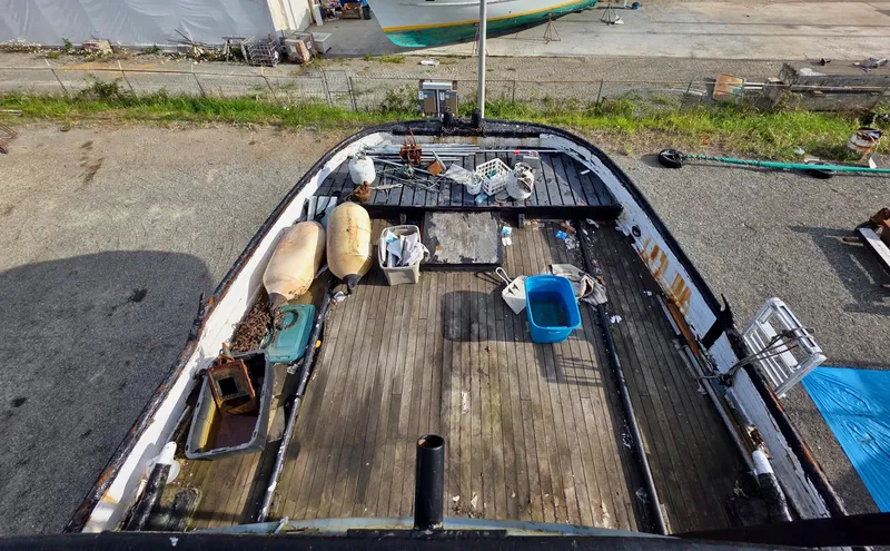 Slide: The Image of Old custom tugboat from 1890 with wooden deck and scattered items, docked on gravel. - 22
