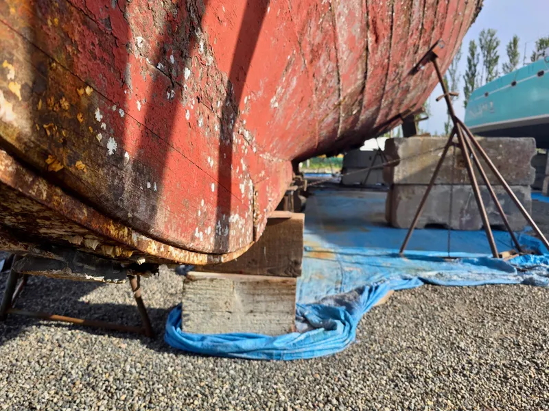 Slide: The Image of Historic 1890 custom tugboat on dry dock, weathered red hull, supported by blocks and tarp. - 46