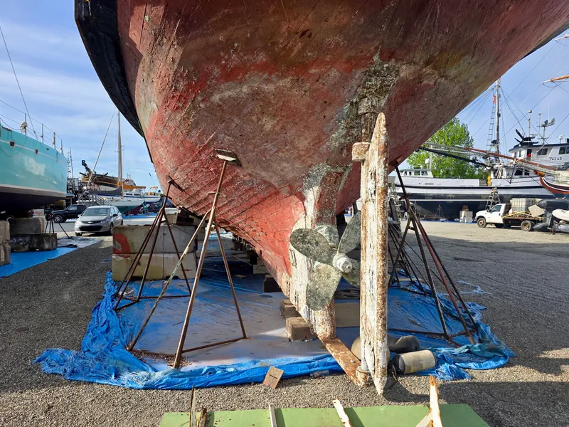 Slide: The Image of Historic 1890 custom tugboat under restoration, supported by stands, on a blue tarp in a shipyard. - 49