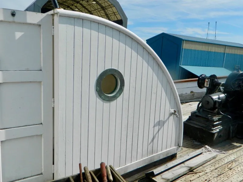 Slide: The Image of Historic 1890 custom tugboat with white wooden structure and porthole, docked near industrial buildings. - 9