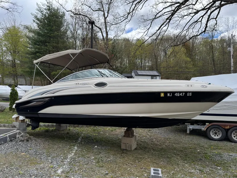 The Image of 2003 Sea Ray 240 Sundeck boat on land with canopy, surrounded by trees. - 0