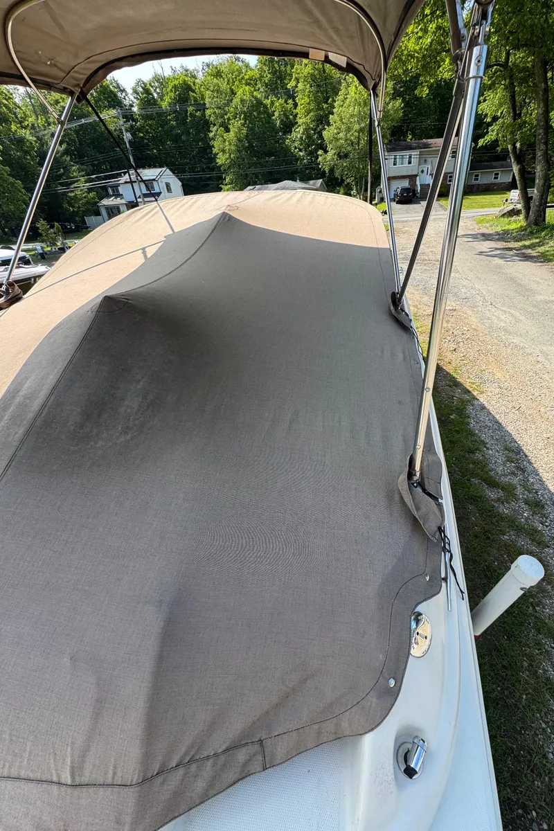 Slide: The Image of 2003 Sea Ray 240 Sundeck with cover, parked outdoors, surrounded by trees and houses. - 18