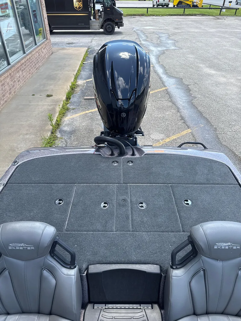 Slide: The Image of 2025 Skeeter ZXR21SE boat interior with motor, parked near a delivery truck. - 26