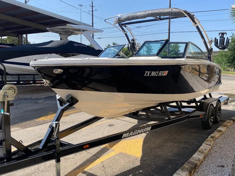Slide: The Image of 2018 Cobalt CS23 Surf boat on a Magnum trailer, parked outdoors. - 4