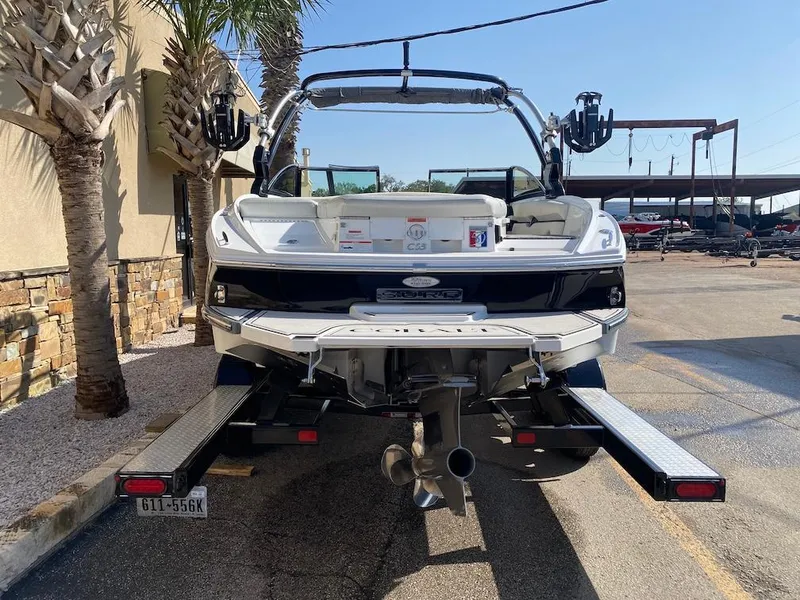 Slide: The Image of 2018 Cobalt CS23 Surf boat on trailer, rear view, parked near palm trees. - 6