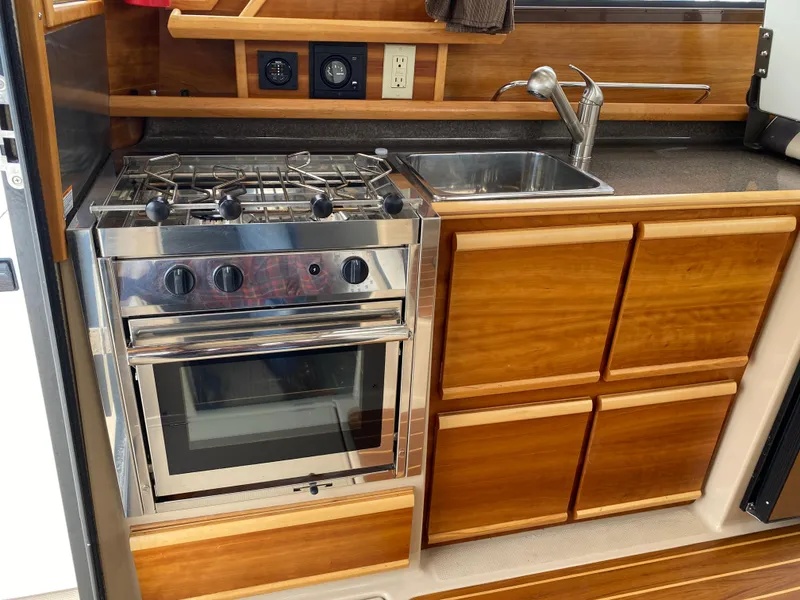 Slide: The Image of 2017 Cutwater C-28 boat kitchen with stove, sink, and wooden cabinetry. - 12