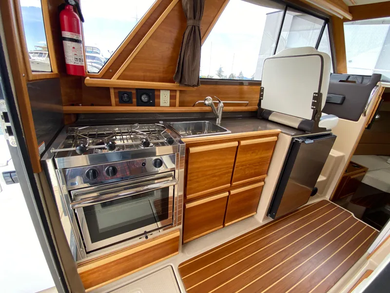 Slide: The Image of 2017 Cutwater C-28 boat interior kitchen with stove, sink, and wooden cabinetry. - 7