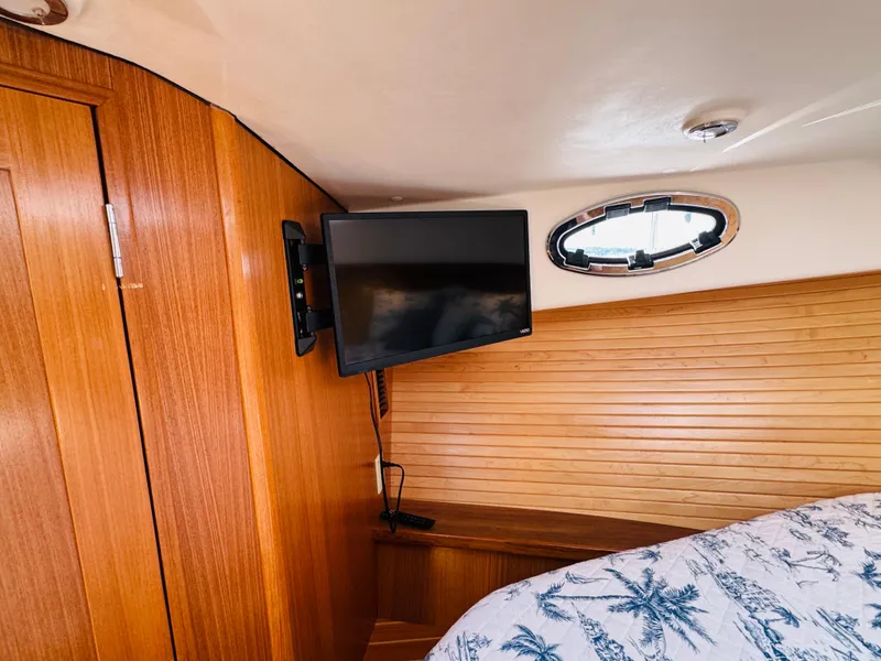 Slide: The Image of 2024 True North 34 Outboard Express cabin with TV, wooden interior, and porthole window. - 18