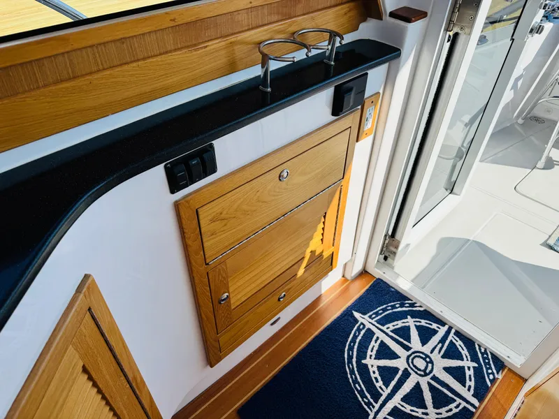 Slide: The Image of 2024 True North 34 Outboard Express interior with wooden cabinetry and nautical-themed rug. - 9