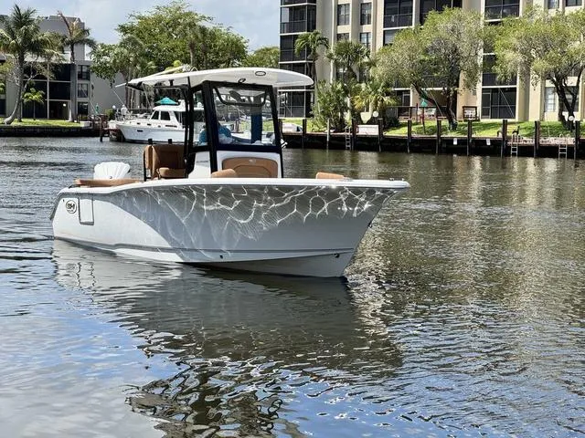 Slide: The Image of 2024 Sea Hunt Ultra 239 SE boat on a calm river near waterfront buildings. - 18