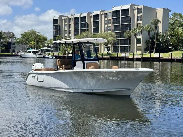 Slide: The Image of 2024 Sea Hunt Ultra 239 SE boat on calm water near modern buildings. - 19
