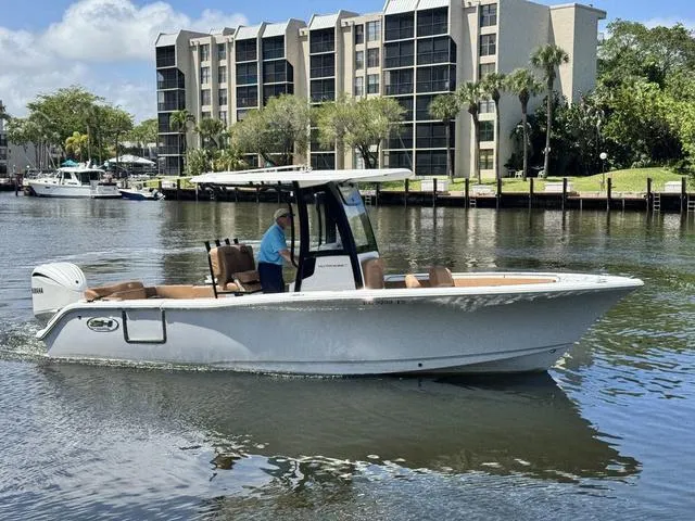 Slide: The Image of 2024 Sea Hunt Ultra 239 SE boat cruising on a calm river near modern buildings. - 23