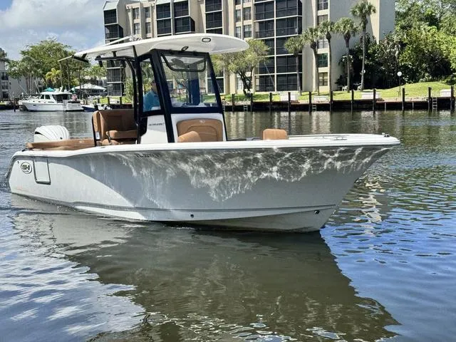 Slide: The Image of 2024 Sea Hunt Ultra 239 SE boat on calm water near waterfront buildings. - 25