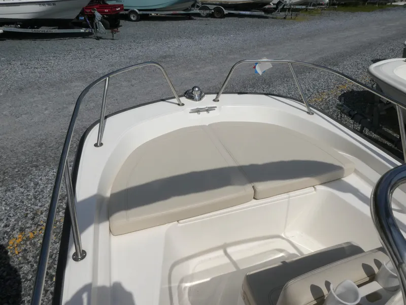 Slide: The Image of 2022 Boston Whaler 150 Montauk boat with cushioned seating, parked on gravel. - 8
