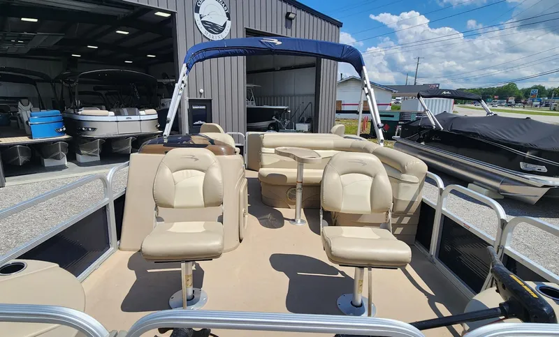 Slide: The Image of 2014 Bennington 20 SF pontoon boat with beige seating and blue canopy, docked near a showroom. - 4