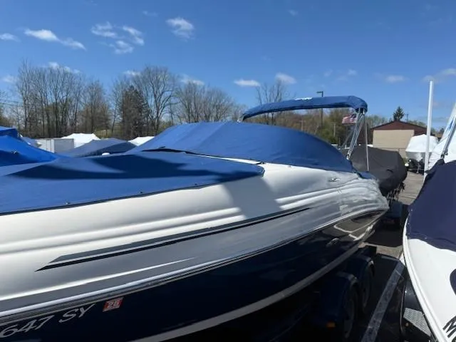 Slide: The Image of 2006 Sea Ray 220 Sundeck boat with blue cover, parked outdoors under clear sky. - 6