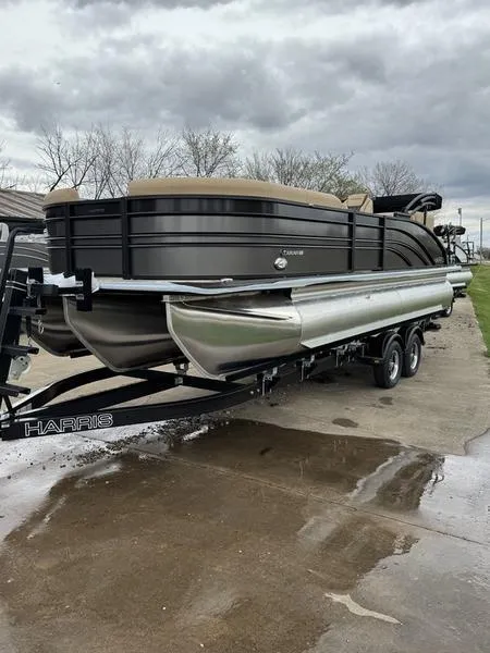 Slide: The Image of 2025 Harris Sunliner 230 pontoon boat on trailer, parked outdoors on a cloudy day. - 2