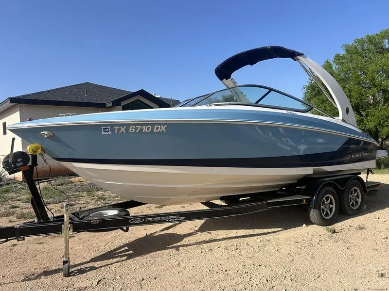 Slide: The Image of 2017 Regal 2300 Bowrider boat on trailer, blue and white, parked outdoors. - 1