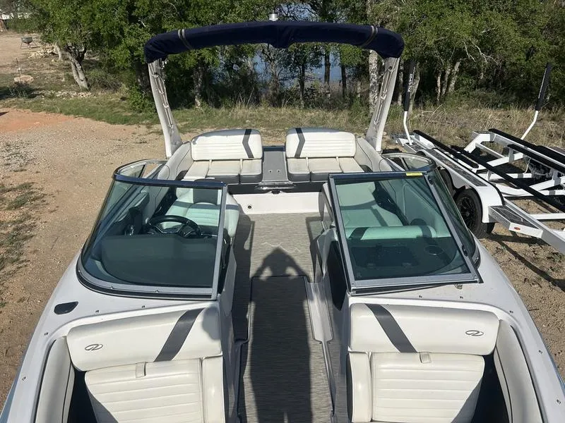 Slide: The Image of 2017 Regal 2300 Bowrider boat with open seating, parked on a trailer, surrounded by trees. - 6