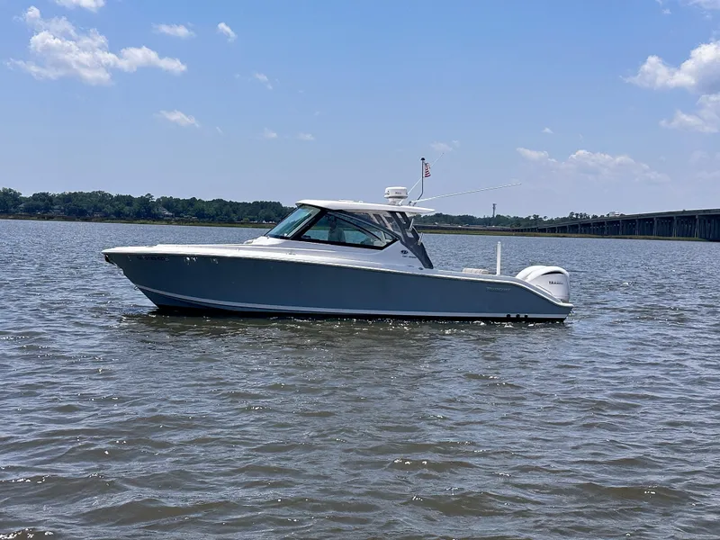 Slide: The Image of 2024 Pursuit DC 295 Dual Console boat on calm water under a clear blue sky. - 3