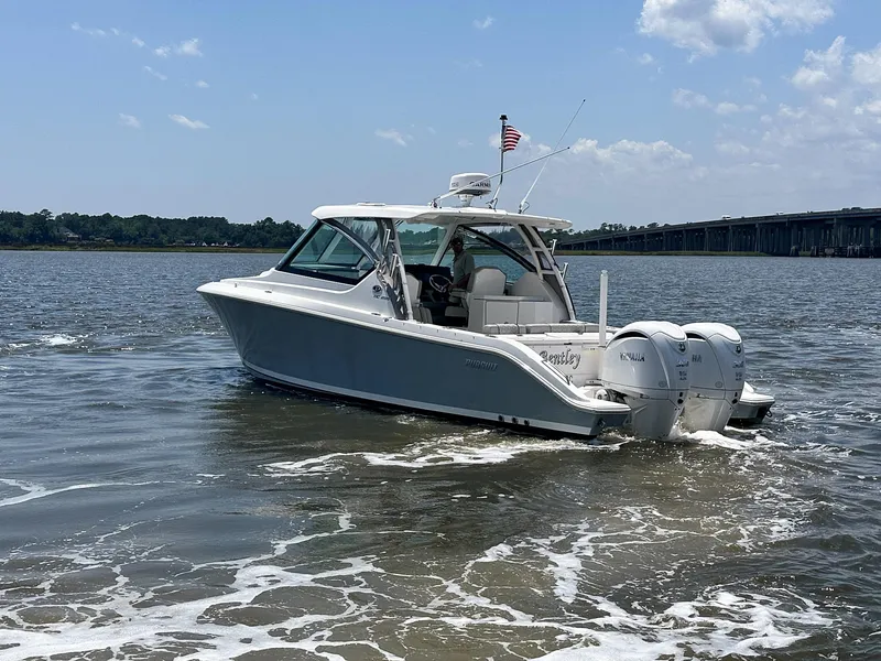 Slide: The Image of 2024 Pursuit DC 295 Dual Console boat cruising on a sunny day with bridge in background. - 5