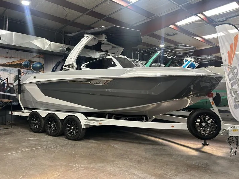 Slide: The Image of 2025 Tigé Ultré 23ZX boat on display in showroom, featuring sleek design and triple-axle trailer. - 0