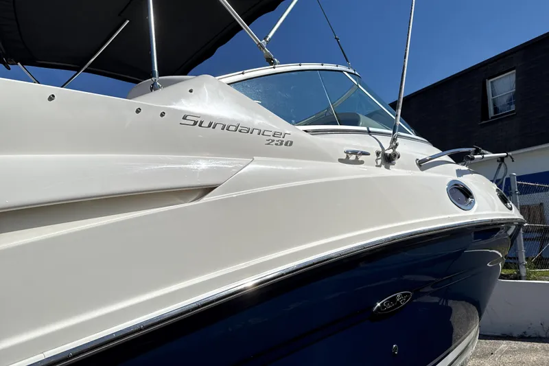 Slide: The Image of 2009 Sea Ray 230 Sundancer boat, sleek design, white and blue exterior, docked under clear sky. - 19