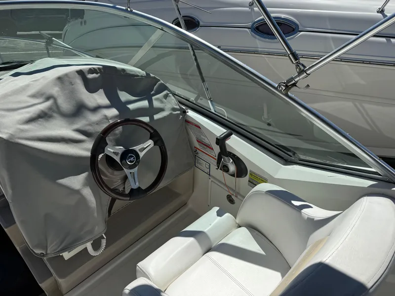 Slide: The Image of 2009 Sea Ray 230 Sundancer boat interior with covered steering wheel and white seating. - 2