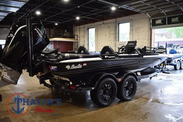 Slide: The Image of 2023 Bass Cat Puma STS boat in showroom, black exterior, dual-axle trailer, indoor lighting. - 7