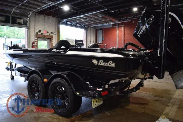 Slide: The Image of 2023 Bass Cat Puma STS boat in a garage, featuring sleek black design and dual axle trailer. - 9