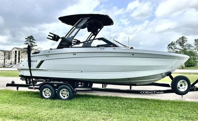 Slide: The Image of 2025 Cobalt R6 Surf boat on trailer, parked on grass under cloudy sky. - 3