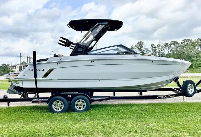 Slide: The Image of 2025 Cobalt R6 Surf boat on trailer, parked on grass under cloudy sky. - 4