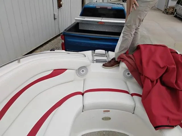 Slide: The Image of 2004 Sylvan 2240 Deck Boat interior with red and white seating, near a blue truck. - 15