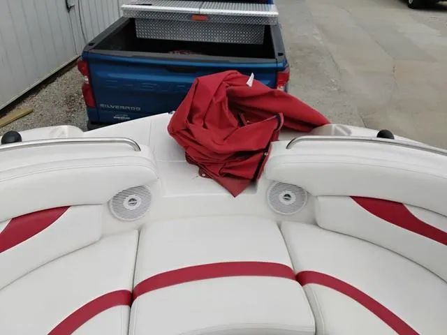 Slide: The Image of 2004 Sylvan 2240 Deck Boat interior with red and white seating, near a blue truck. - 5