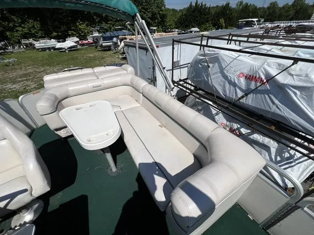 Slide: The Image of 1999 Sanpan 2500R pontoon boat with white seating and table, parked outdoors. - 8