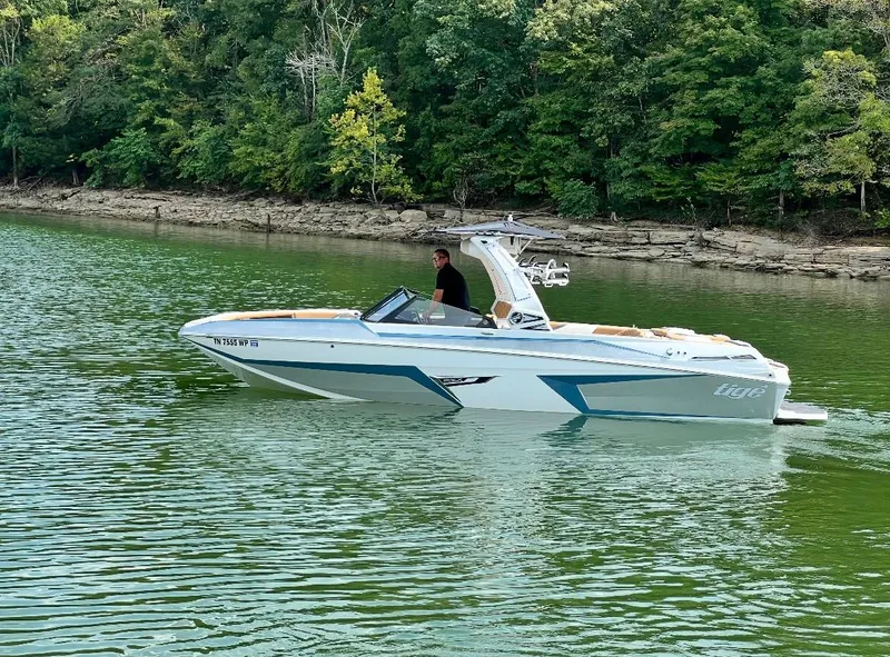 Slide: The Image of 2022 Tigé 24RZX boat cruising on a serene lake with lush green forest backdrop. - 0