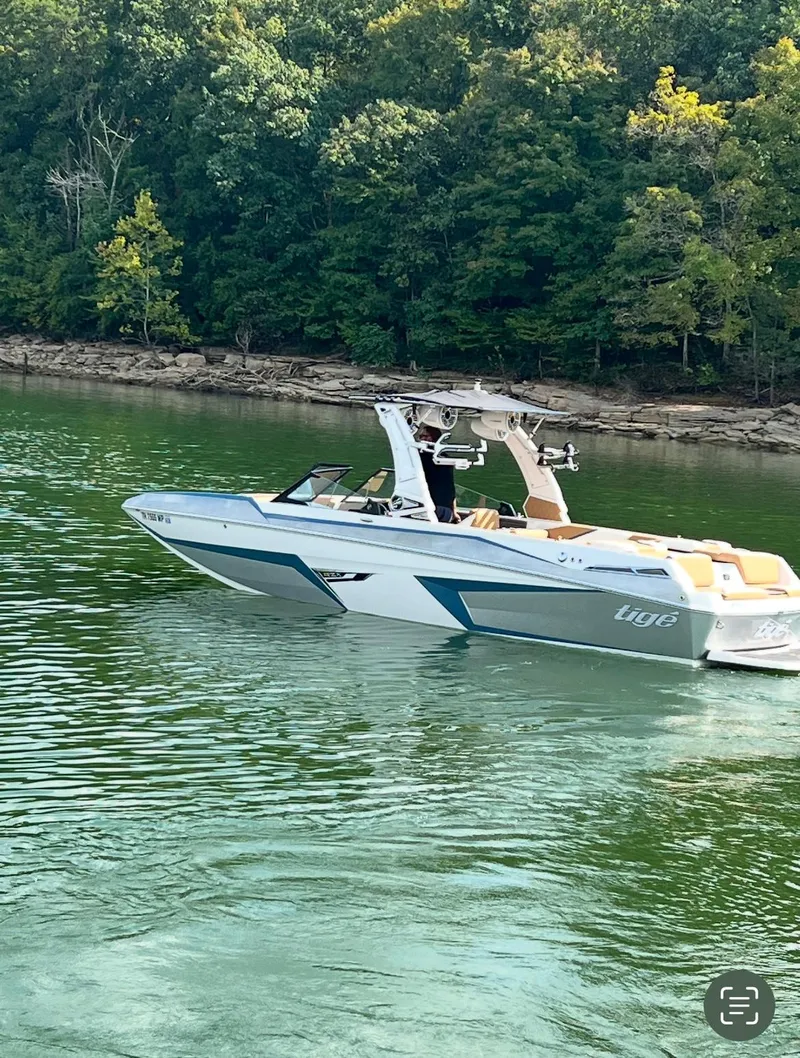 Slide: The Image of 2022 Tigé 24RZX boat cruising on a serene lake with lush green forest backdrop. - 1