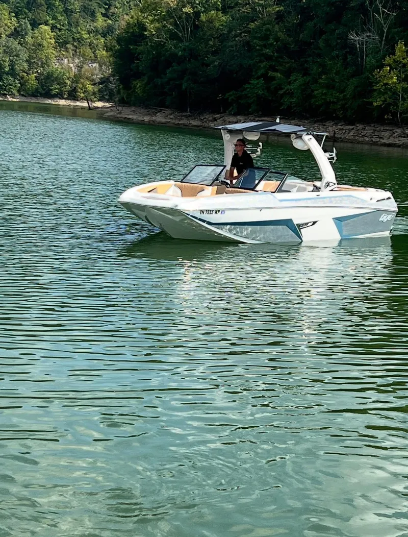 Slide: The Image of 2022 Tigé 24RZX boat on a serene lake with lush green surroundings. - 2