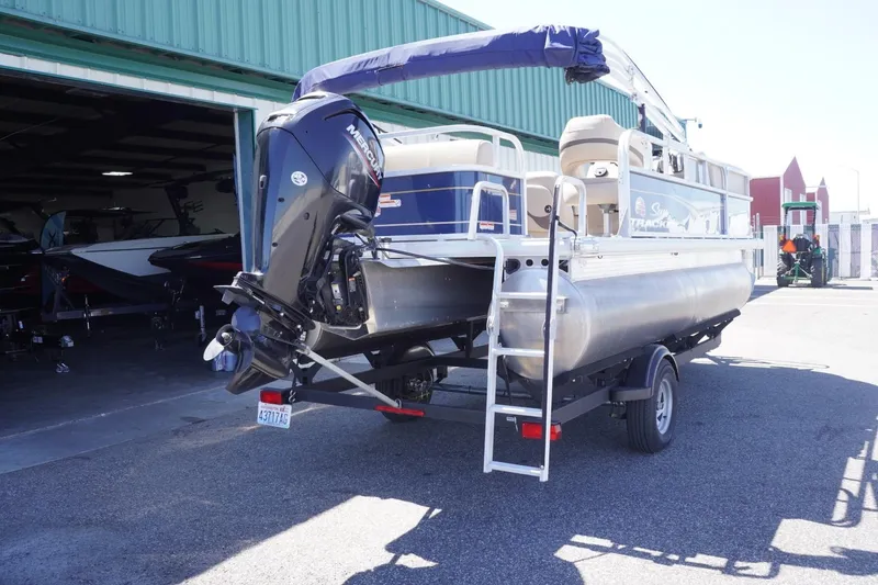 Slide: The Image of 2022 Sun Tracker Party Barge 18 DLX pontoon boat on trailer, parked outside a green building. - 11