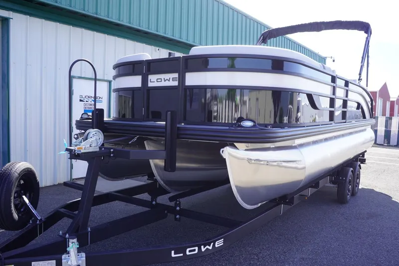 Slide: The Image of 2025 Lowe SS 230 DL pontoon boat on trailer, parked outside a building. - 17