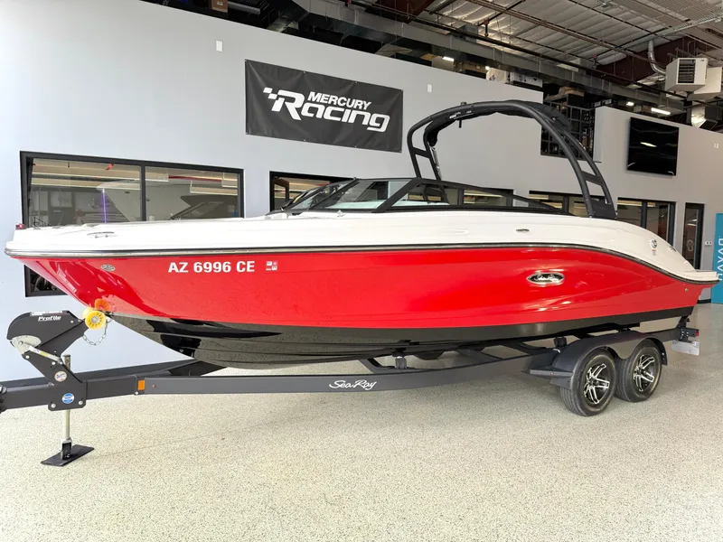 The Image of 2024 Sea Ray SPX230 boat in showroom, red hull, on trailer, Mercury Racing sign above. - 1