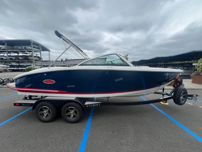 Slide: The Image of 2023 Cobalt CS22 boat on trailer, parked in marina lot under cloudy sky. - 1