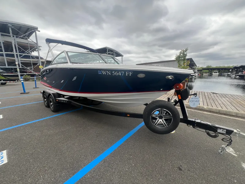 Slide: The Image of 2023 Cobalt CS22 boat on trailer, parked near waterfront, overcast sky. - 2