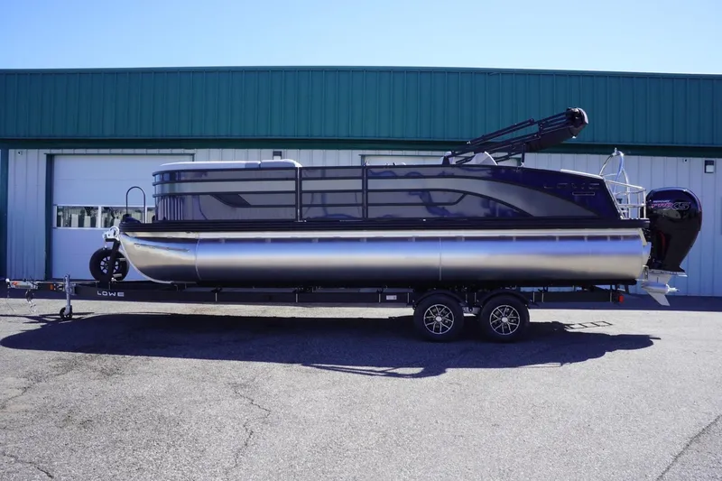 Slide: The Image of 2025 Lowe SS 230 DL pontoon boat on trailer, parked outside a green building. - 1