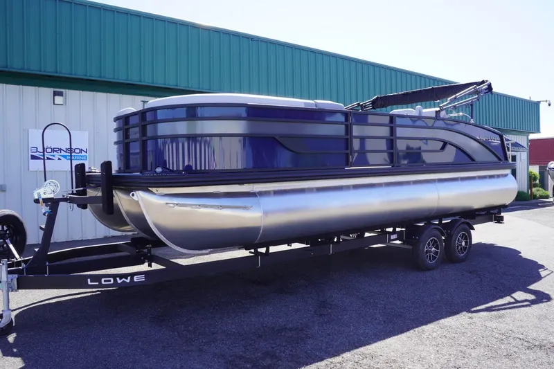 Slide: The Image of 2025 Lowe SS 230 DL pontoon boat on trailer outside a green building. - 2
